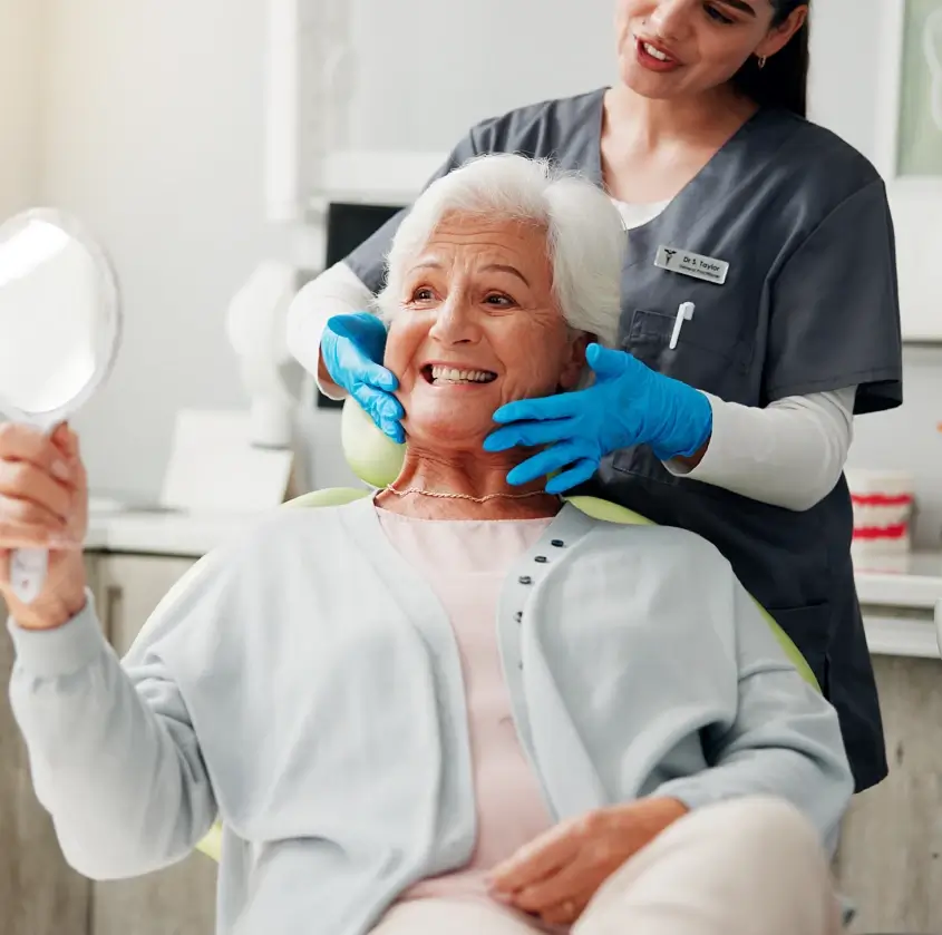 A senior patient admiring her smile in a hand mirror