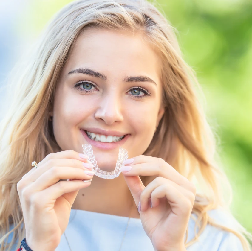 A smiling young woman holding a clear aligner