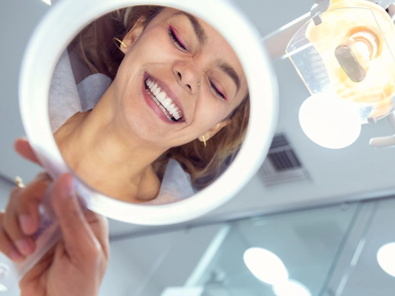A patient admiring her new smile in a hand mirror at the dental office